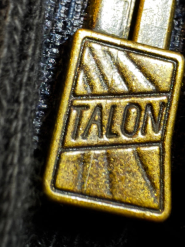 Close-up of a gold belt buckle with 'Talon' branding on a black background