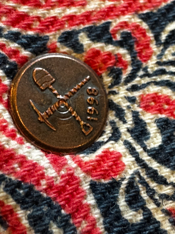 Bronze coin with '8661' marking on a fabric background with red, blue, and white pattern