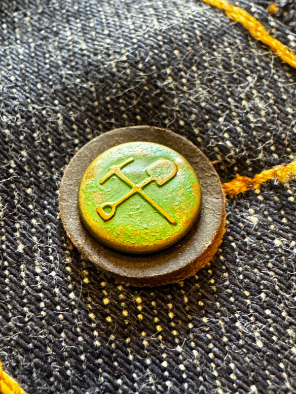 Vintage button with a green and gold emblem on denim fabric