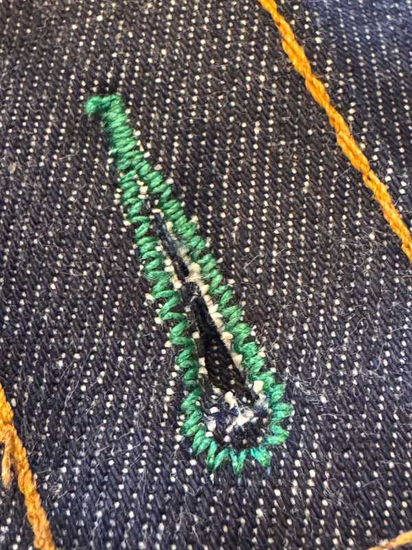 Embroidered design on a denim fabric with green thread and black needle.