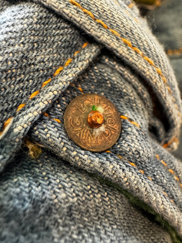 Close-up of a button on a denim jacket with visible stitching details.