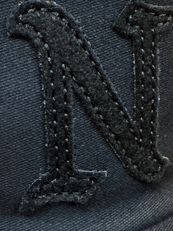 Close-up of a black embroidered letter 'N' patch on a dark navy fabric background.