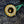 Close-up of a decorative brass button with floral engraving, set into dark textured fabric with a green thread tail visible on the right.