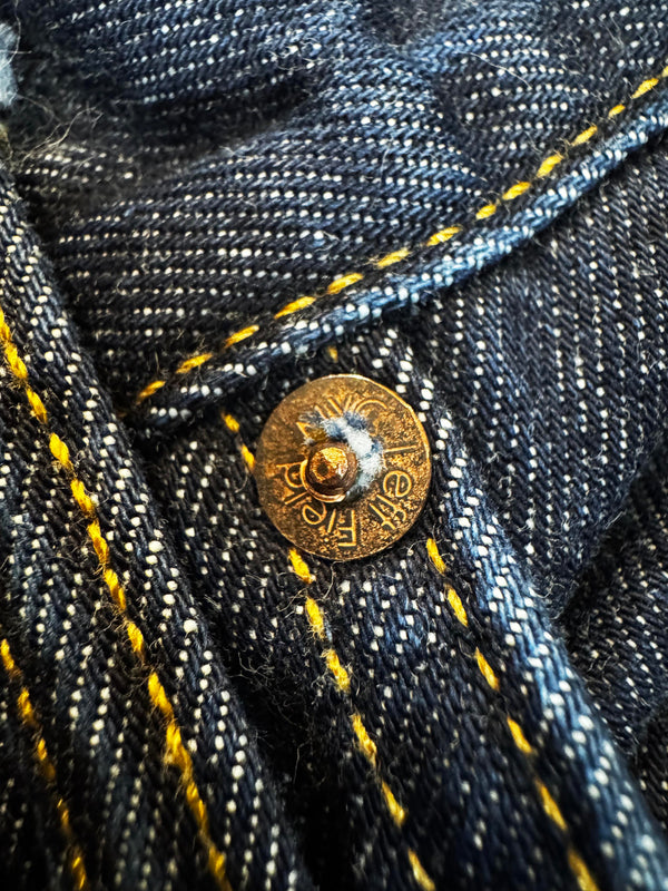 Close-up of a gold button on dark denim fabric with yellow stitching.