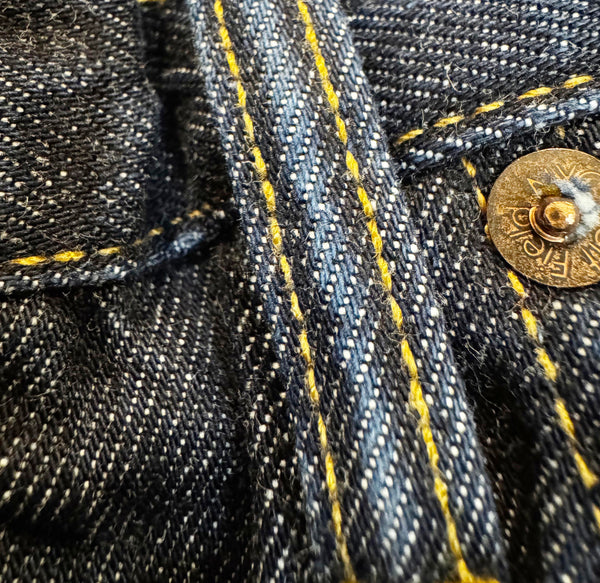 Close-up of denim fabric with yellow stitching and a button.