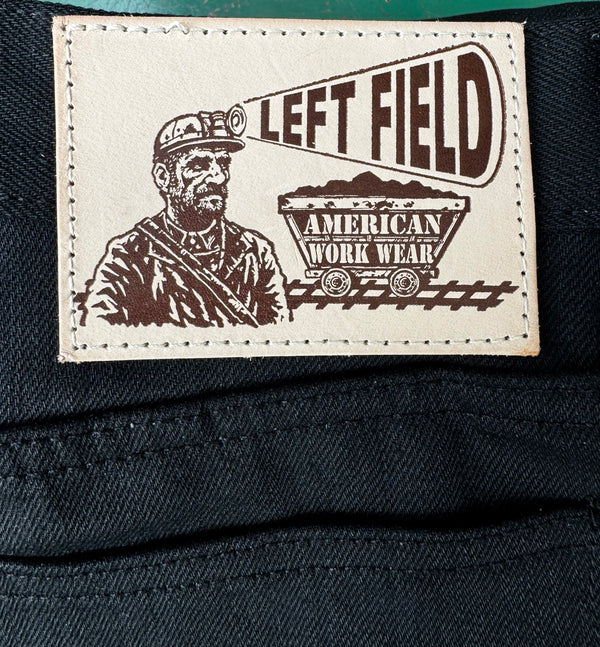 Close-up of a 'Left Field' American work wear label on a dark fabric background.