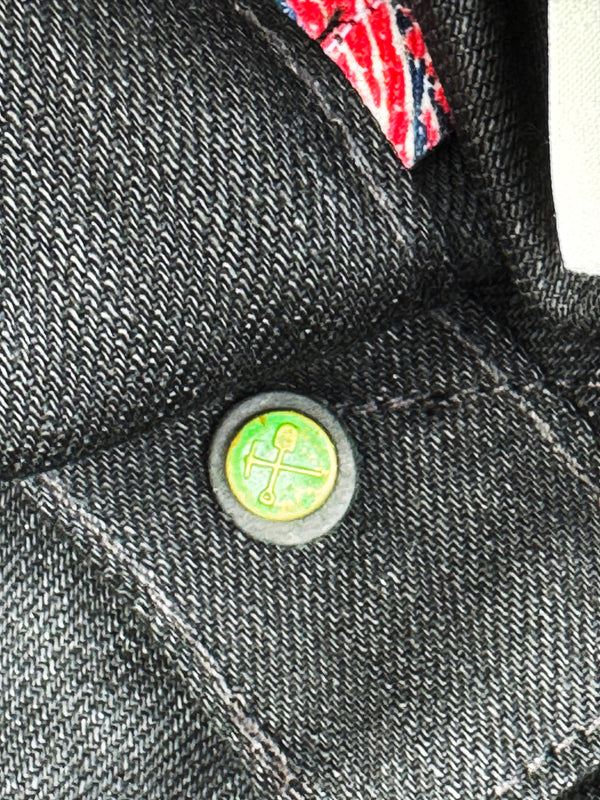 Close-up of a button on a denim jacket with a small flag in the background
