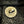 A close-up of a round brass button stamped with the words 'Left Field' on a dark textured denim fabric.