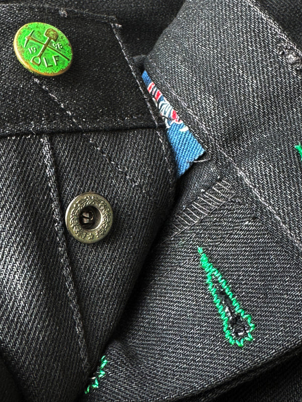 Close-up of a black denim jacket with a button, embroidered design, and brand label.