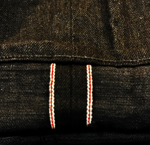 Close-up of dark indigo denim fabric with two vertical red and white contrast stitching lines.