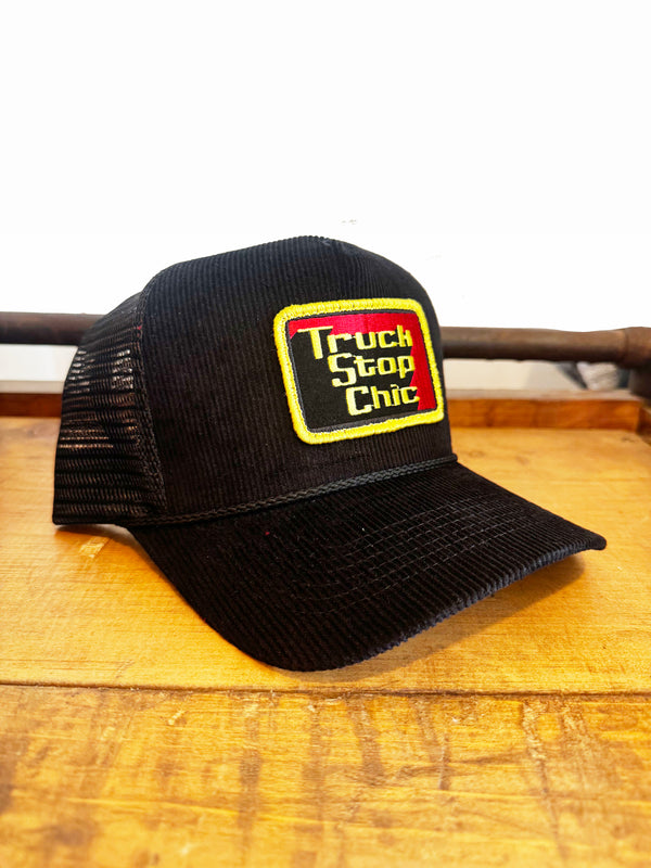 Black trucker hat with 'Truck Stop Chic' logo on a wooden surface