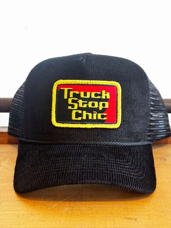 Black trucker hat with 'Truck Stop Chic' patch on a wooden surface