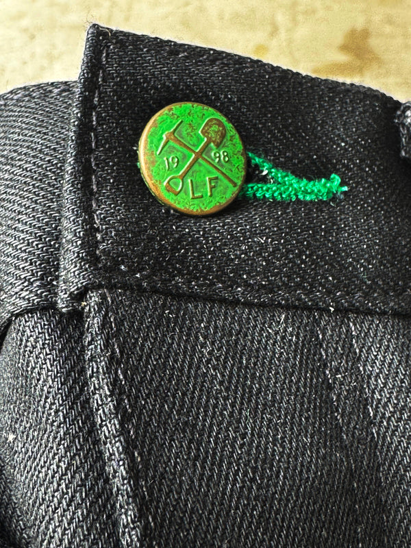 Green lapel pin on a dark suit jacket with a beige background