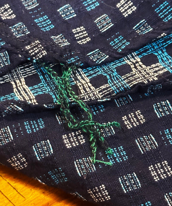 Close-up of patterned fabric with green thread on a wooden surface