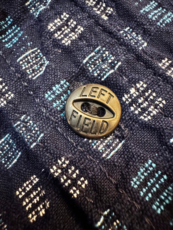 Bronze button with 'LEFT FIELD' text on a textured fabric background