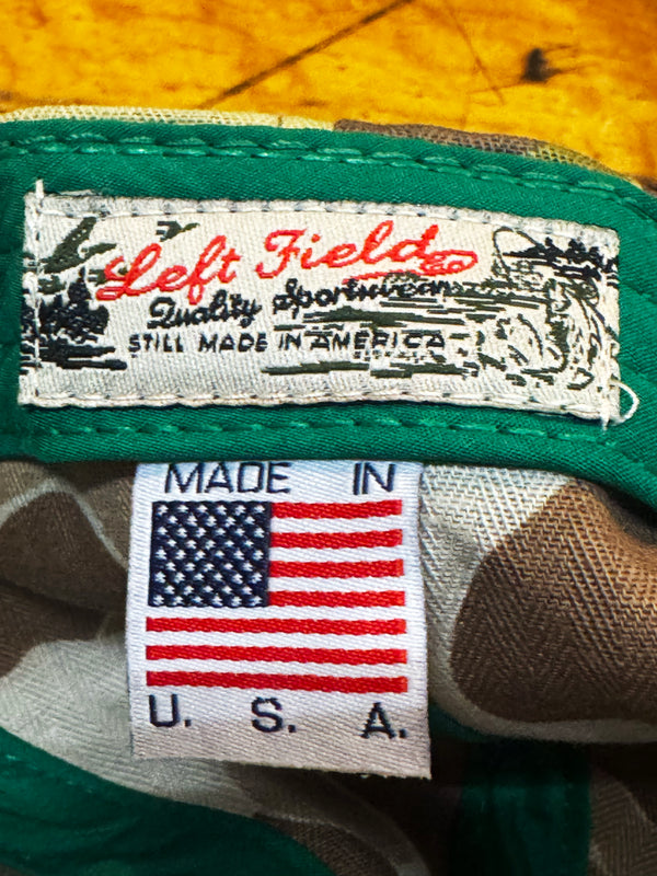Close-up of a green and camouflage fabric item showing two tags: a main white label reading 'Left Field Quality Sports' and a smaller 'MADE IN U.S.