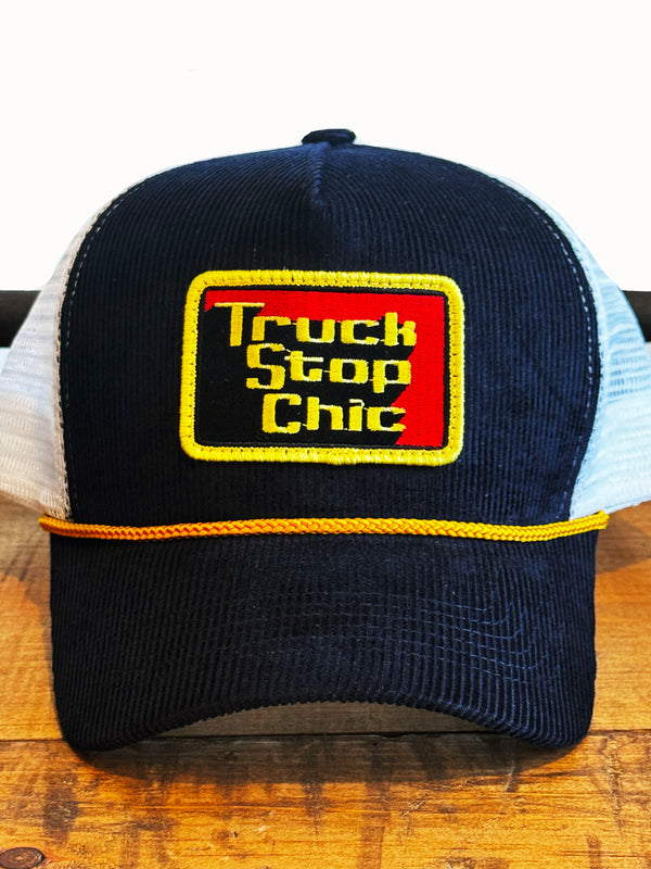 Navy blue and white trucker hat with 'Truck Stop Chic' logo on a wooden surface