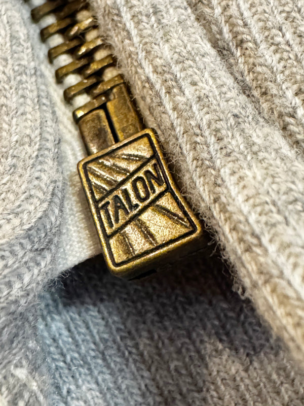 Close-up of a brass zipper pull with 'Talon' branding on a textured fabric background.