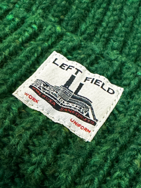 Close-up of a 'LEFT FIELD' label on a green textured fabric background