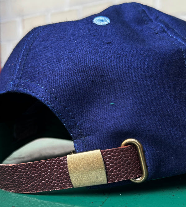 Blue cap with a brown leather strap on a tiled surface
