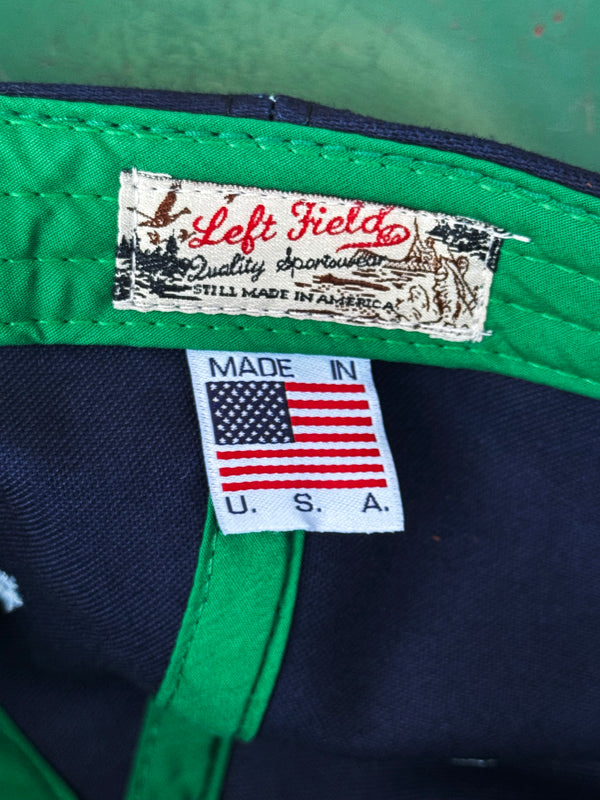 Close-up of a green and navy cap with 'Left Field' label and 'Made in USA' tag.