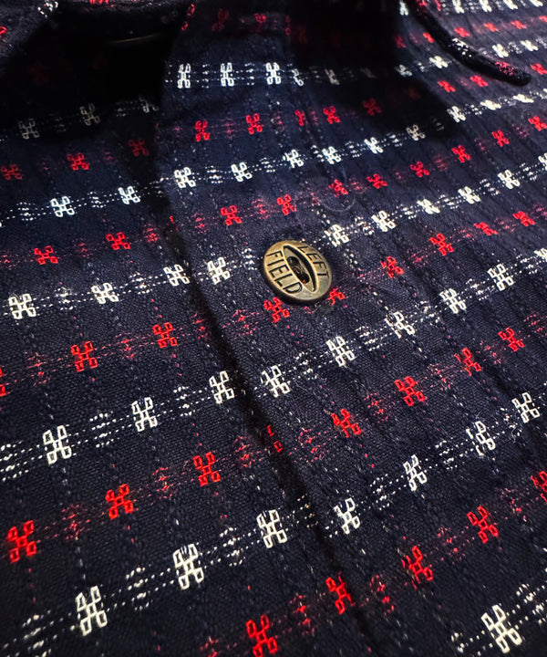 Close-up of a patterned shirt with a button, featuring red, white, and blue colors.