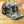A baseball cap with a green, brown, and beige camouflage pattern, featuring a black embroidered 'LA' on the front, resting on a wooden floor.