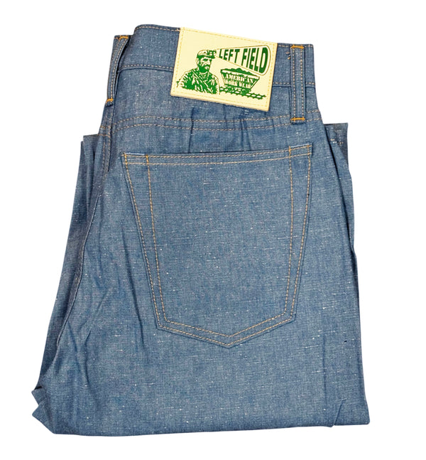 A pair of folded blue denim jeans with a yellow 'The Left Field' brand patch visible at the waistband, shot against a plain white background.