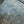 Close-up of dark blue denim fabric with visible yellow contrast stitching and small lint or fiber particles on the surface.