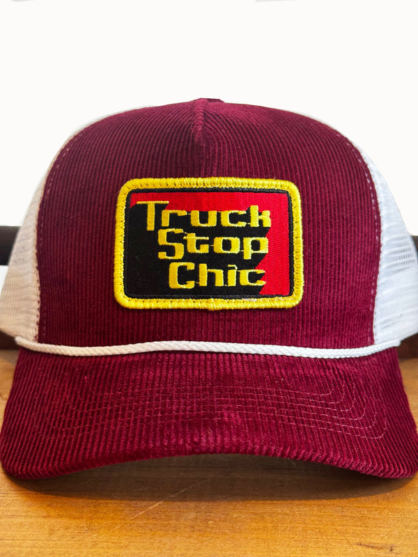 Maroon and white trucker hat with 'Truck Stop Chic' logo on a wooden surface.