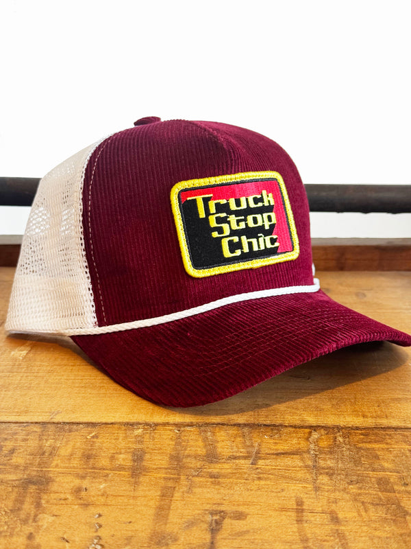 Maroon and beige trucker hat with 'Truck Stop Chic' logo on a wooden surface