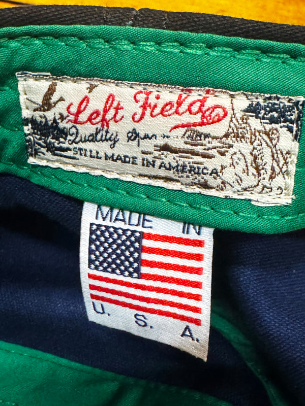 Close-up of a garment's interior labels, showing a green and navy fabric lining with a sewn-in 'Left Field' brand label and a separate 'MADE IN U.S.