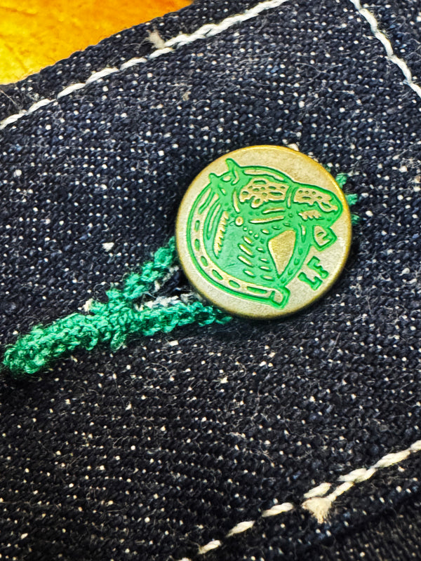 Close-up of a green button with a design on black denim fabric.