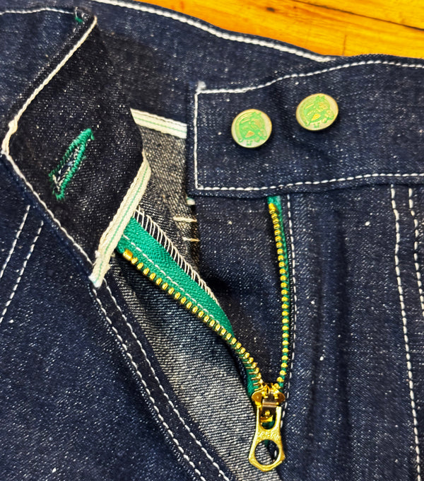 Close-up of a blue denim jacket with a green zipper and gold buttons.