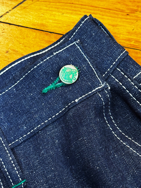 Close-up of a blue denim fabric with a green button on a wooden surface